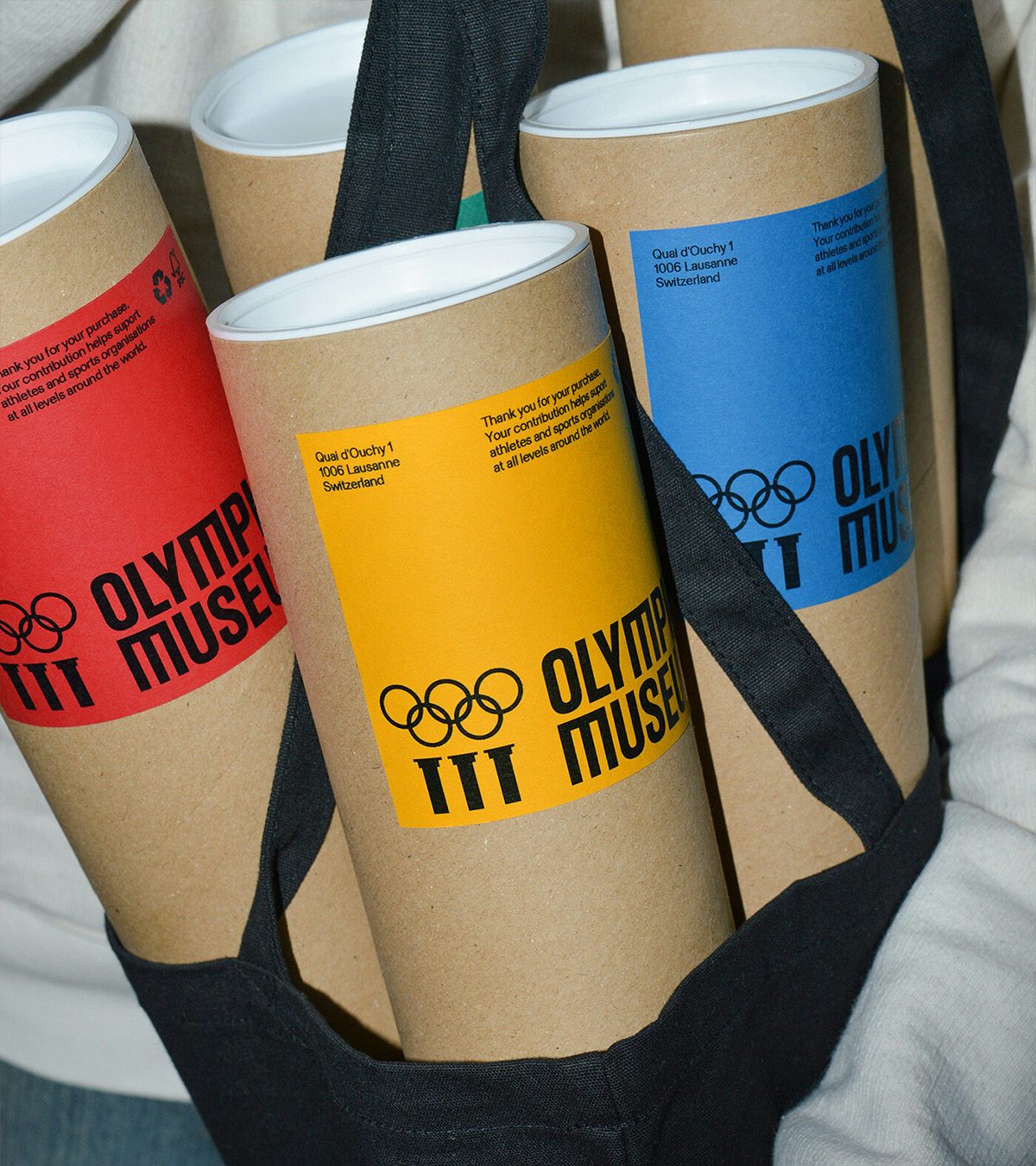 Tubes d'affiches arborant la nouvelle identité du Musée Olympique avec des étiquettes rouges, jaunes et bleues