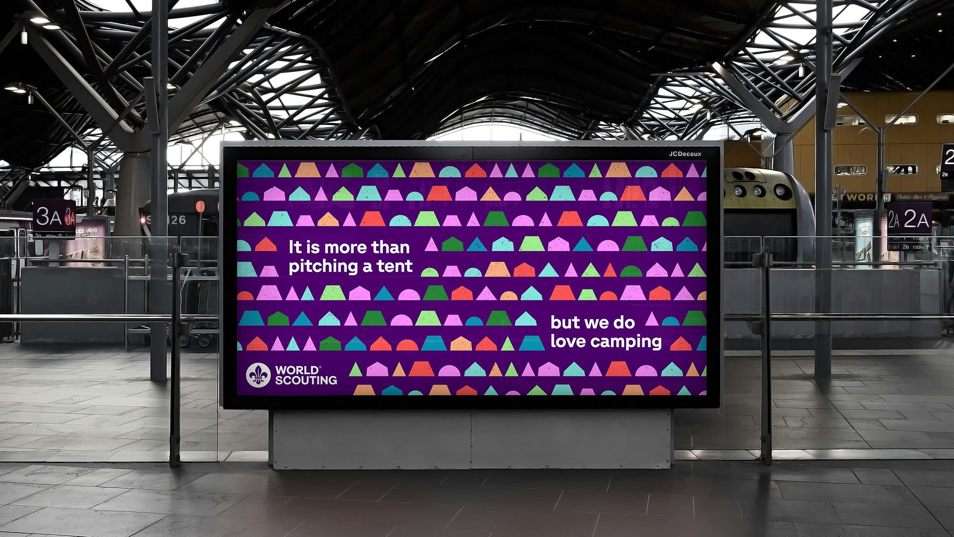 Un affichage numérique pour le Scoutisme mondial avec la phrase « c'est plus que monter une tente, mais nous aimons camper » sur un fond coloré de formes géométriques