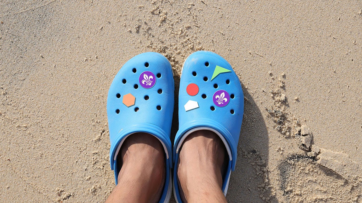 Crocs bleus avec badges du Scoutisme mondial, dont l'emblème de la fleur de lys violette
