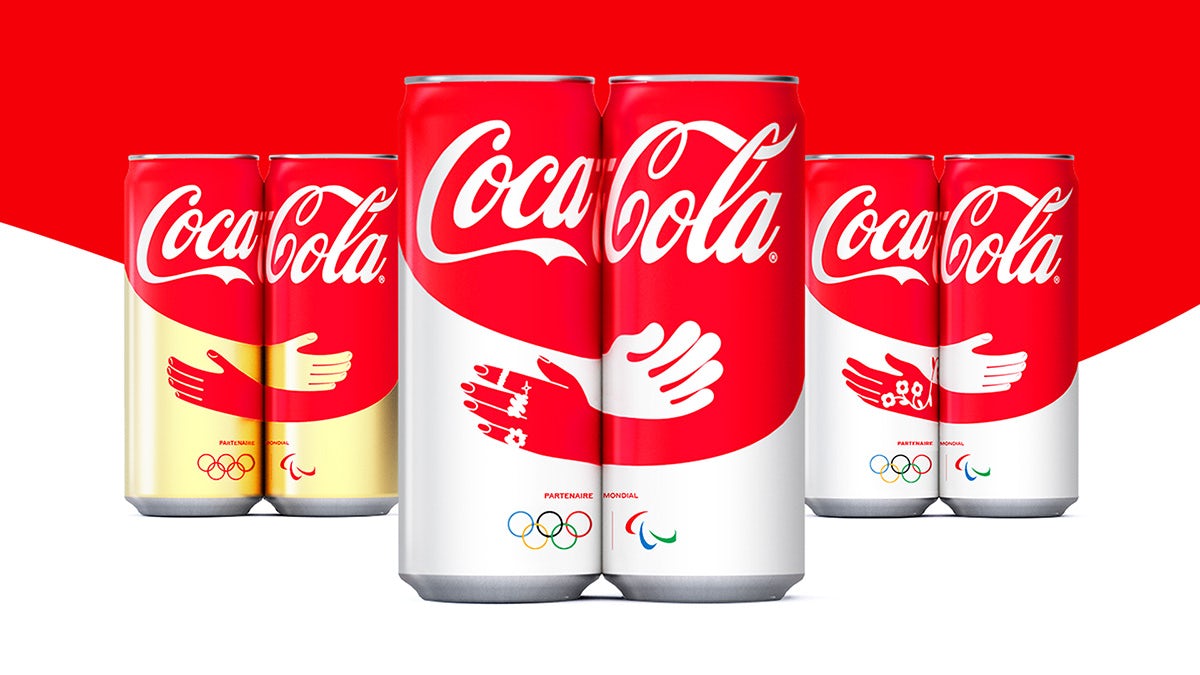 Alignement de trois paires de canettes de Coca-Cola, chacune affichant une illustration de mains s'embrassant sur deux canettes lorsqu'elles sont placées ensemble par paires, créée pour les Jeux olympiques de Paris 2024